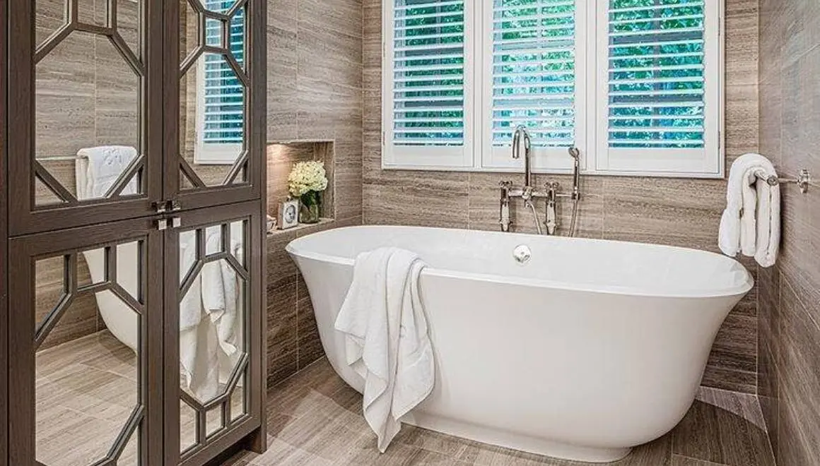 A bathroom with a tub, mirror and window.